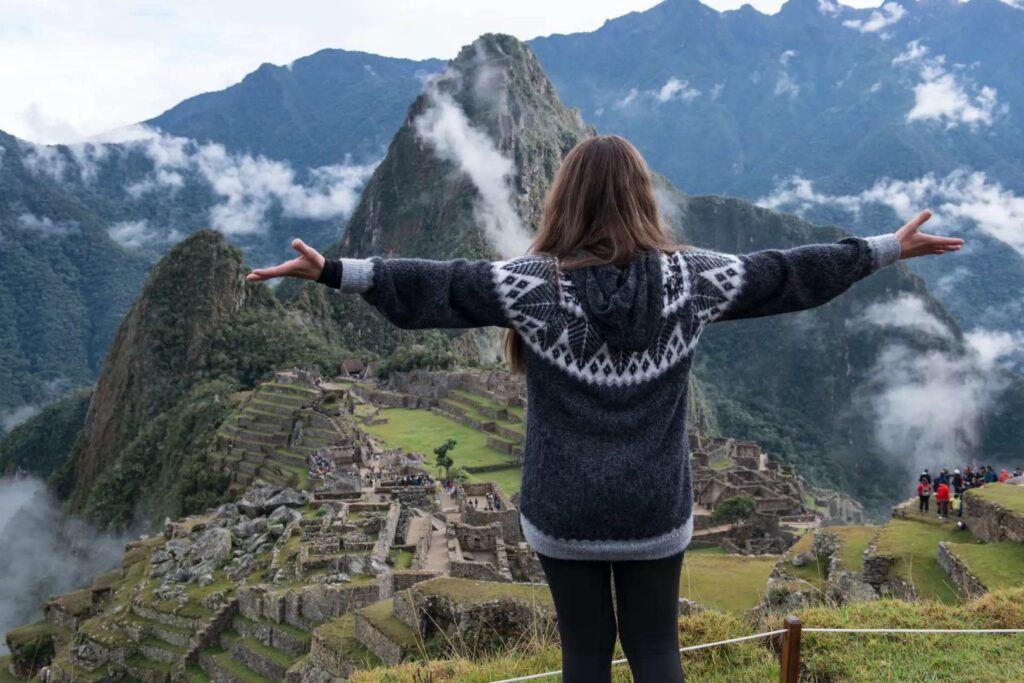 Woman with arms open looking over the ancient ruins of Machu Picchu and mountains.