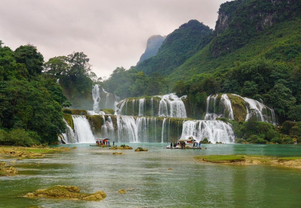 a waterfall in the middle of green mountains on a cloudy day