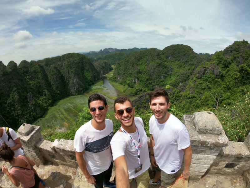 three guys take a selfie with green mountains in the background