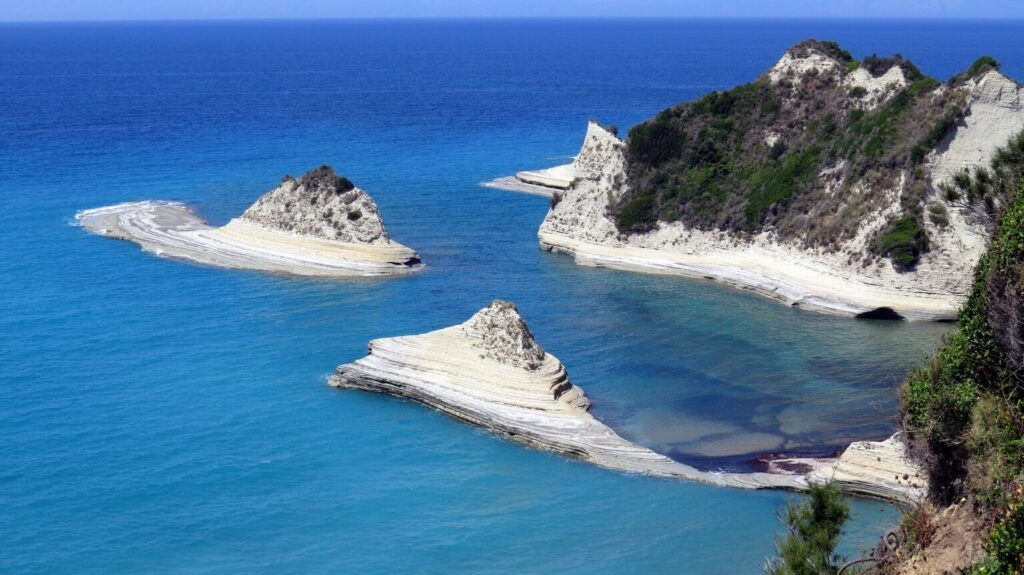 white rocks with green vegetation surrounded by an azure sea