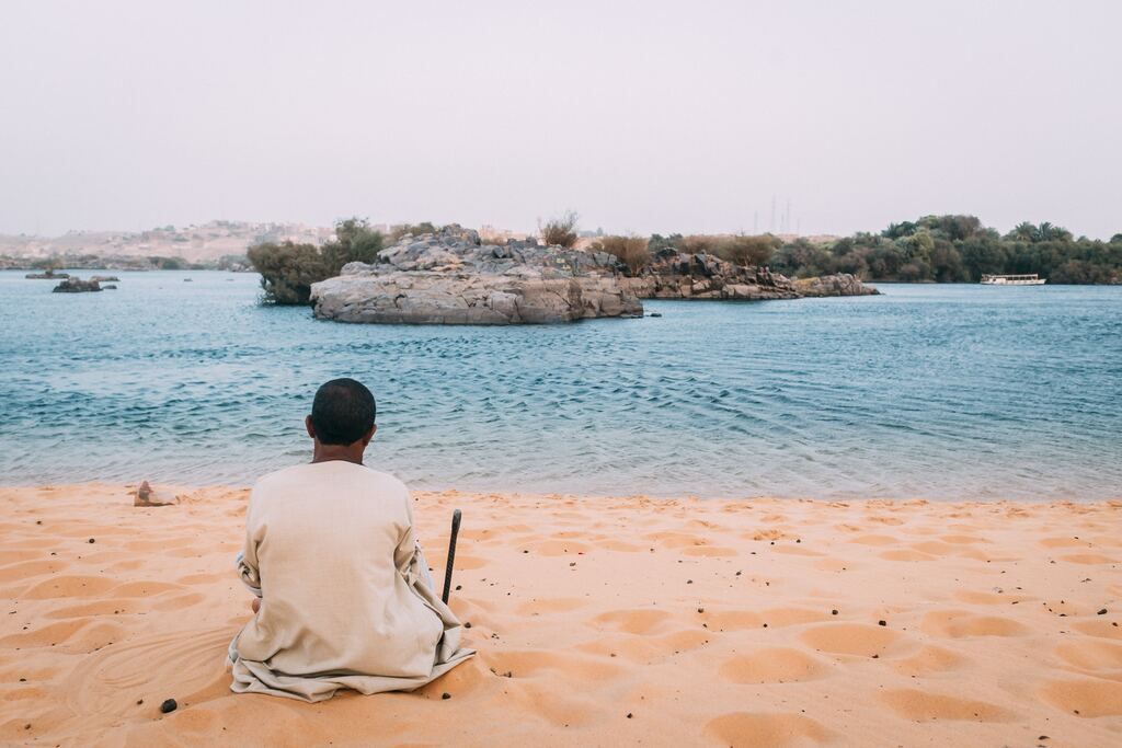 Man sits on sand dunes while looking at the beach.