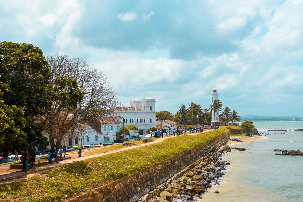 A group of people walking on a pavement next to a body of water in Sri Lanka