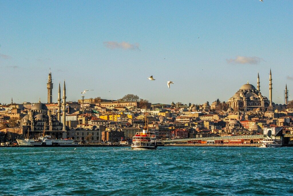 A ferry sails across the Bosphorus in Istanbul, with the city's historic skyline and grand mosques visible in the background.