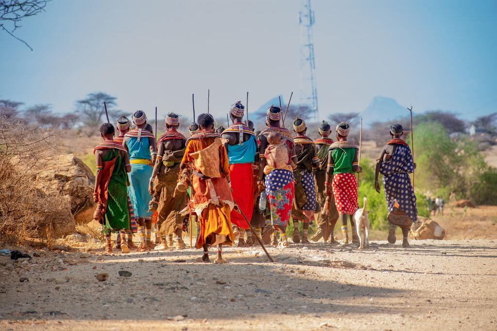 People in traditional orange and yellow dress walking on the brown sand during the day.