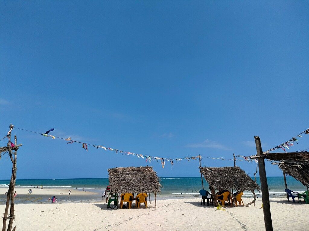A sandy beach with chairs and thatched huts.