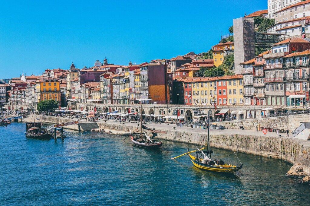 A view of the colorful riverfront buildings in Porto with traditional Rabelo boats anchored in the Douro River.