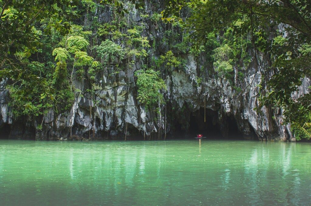 person in red shirt standing on rock in the middle of lake during daytime.
