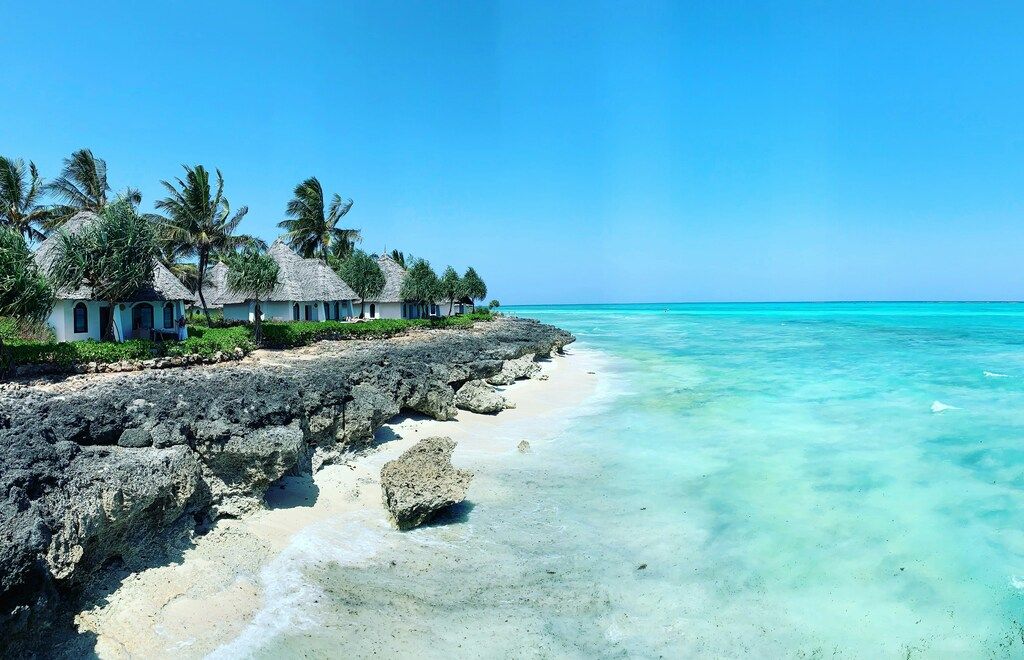 Rocky beach with white cottages under clear blue sky.