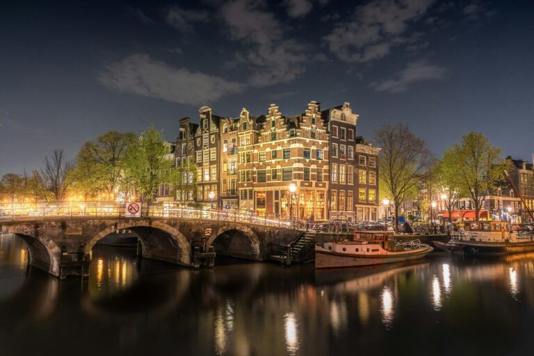 A beautifully lit canal in Amsterdam at night with classic Dutch buildings and boats.