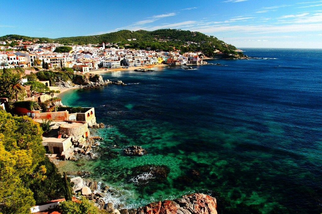 A picturesque coastal town with white houses nestled along a turquoise bay on the rugged Costa Brava in Spain.
