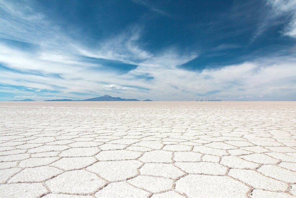 The vast, hexagonal cracked salt flats of Salar de Uyuni in Bolivia stretching to the horizon under a wide blue sky with scattered clouds.