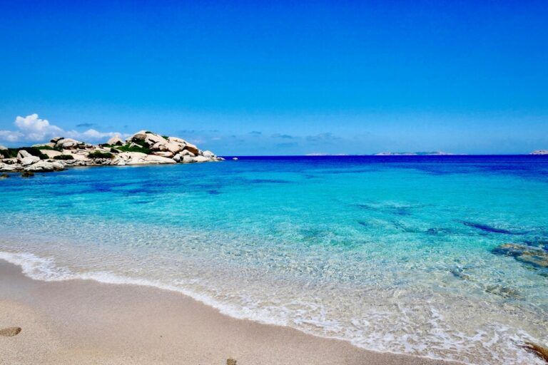 A pristine beach in Sardinia with crystal-clear turquoise waters, white sand, and smooth rocky formations under a bright blue sky