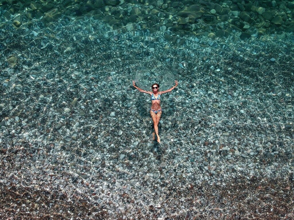 A woman in a bikini relaxes and floats in the clear, turquoise waters of Bečići Beach