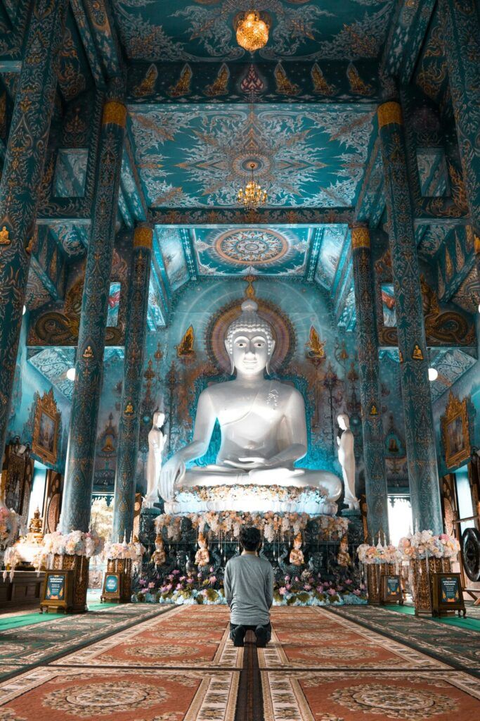 A person kneeling in prayer inside a beautifully ornate Thai temple