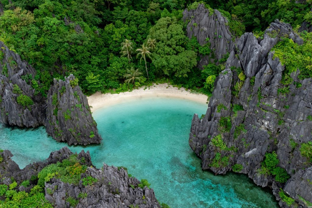 Hidden white sand cove in the Philippines, surrounded by towering black limestone karsts and lush jungle, illustrating an island dupe.
