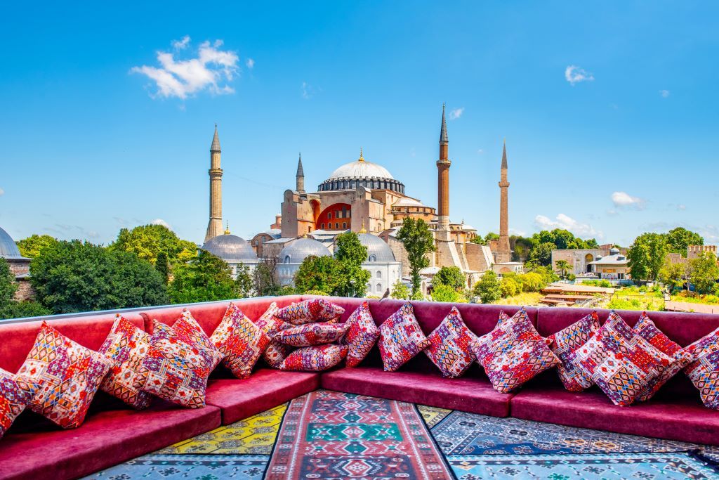 A rooftop terrace with colorful cushions and patterned rugs overlooking the majestic Hagia Sophia in Istanbul.