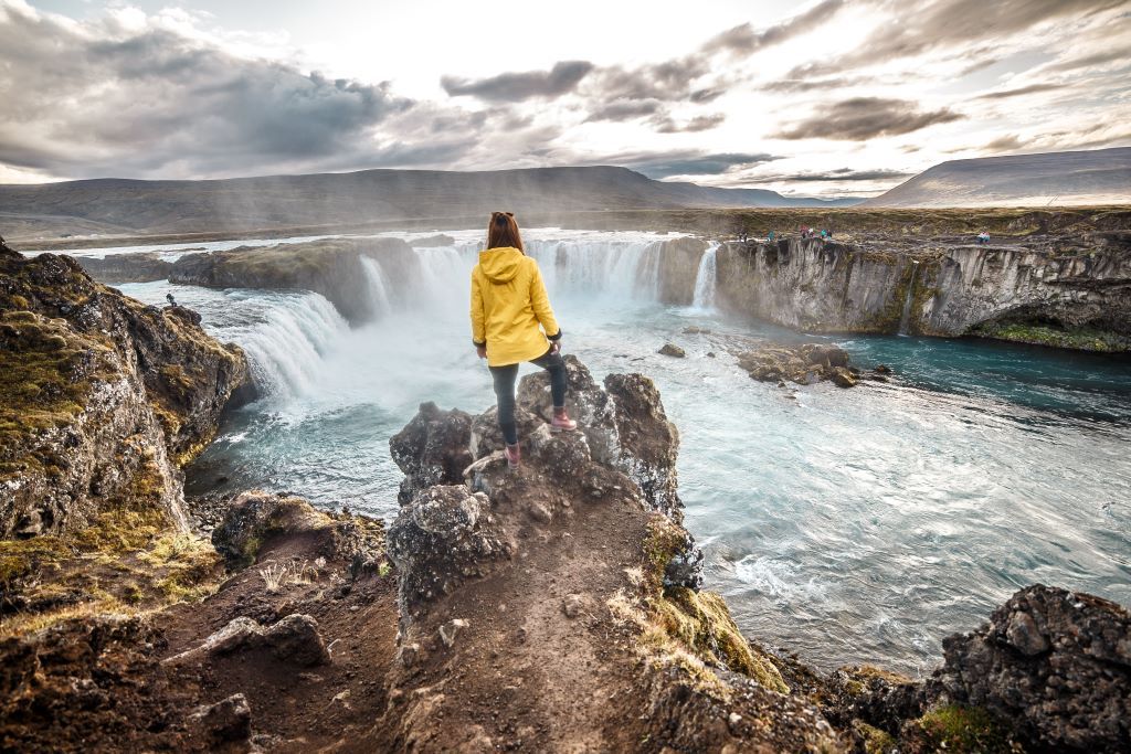 Woman in yellow jacket viewing the powerful waterfall in Iceland.