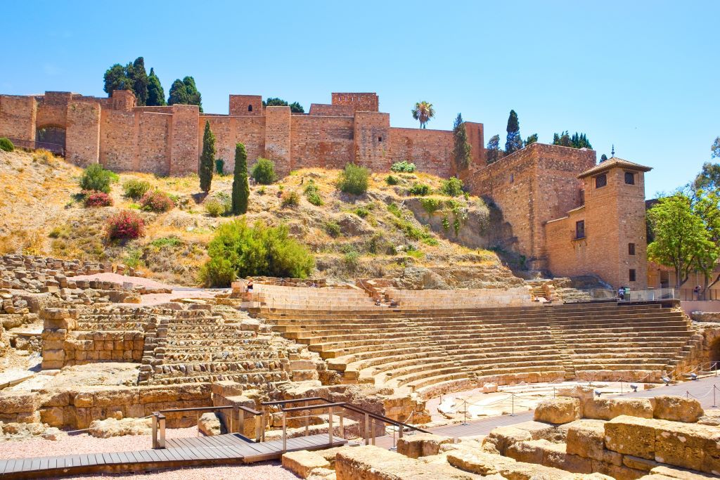 The ancient Roman Theatre of Malaga situated at the foot of the Alcazaba fortress under a clear blue sky.