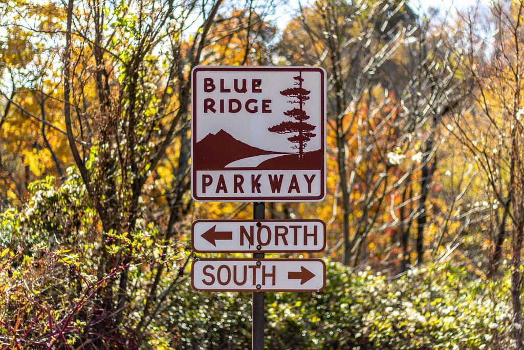 Scenic road sign indicating directions along the Blue Ridge Parkway, surrounded by autumn foliage.