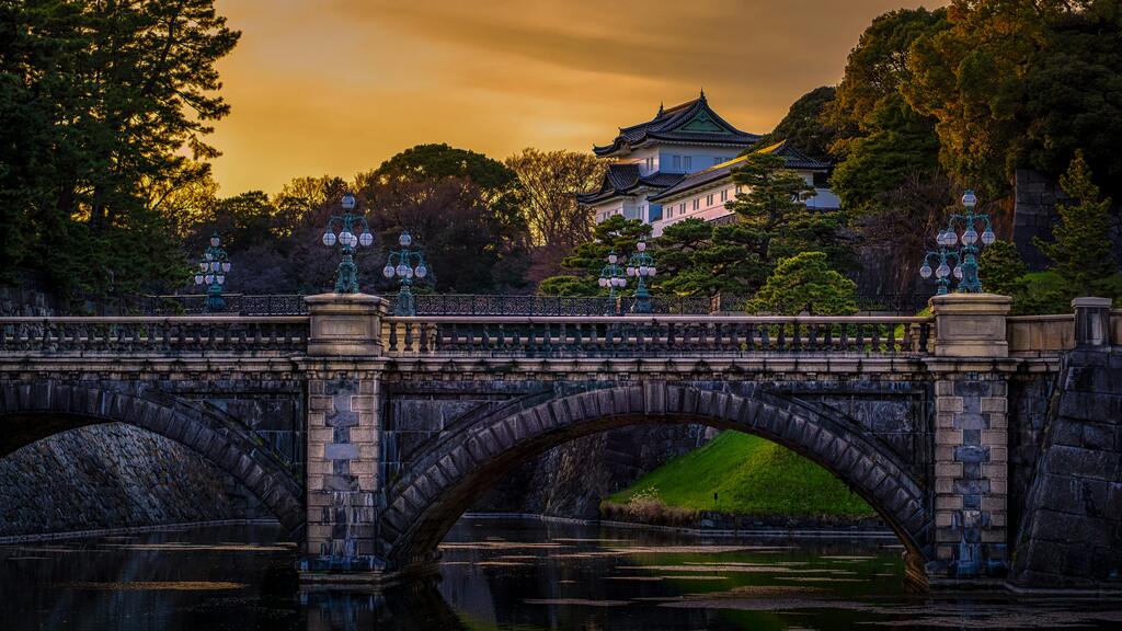 Historic stone bridge (Meganebashi or Eyeglass Bridge) leading toward the Imperial Palace grounds in Tokyo, Japan, at sunset.