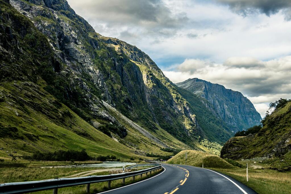 Scenic road winding through dramatic mountains and green valleys in Norway, perfect for a road trip.