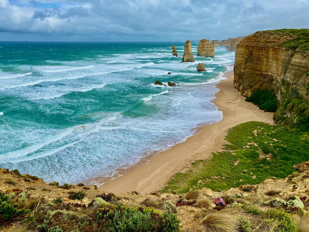 Dramatic view of the Twelve Apostles sea stacks and cliffs on the Great Ocean Road, with turquoise waves crashing onto a sandy beach.