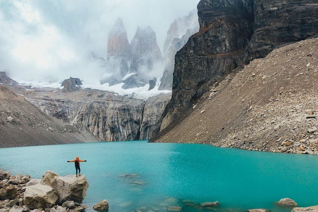 Hiker with arms open facing a bright turquoise glacial lake and the Torres del Paine mountains in Patagonia.