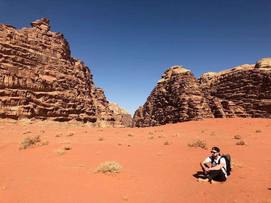 A traveler sits on the red sand of the Wadi Rum desert in Jordan.