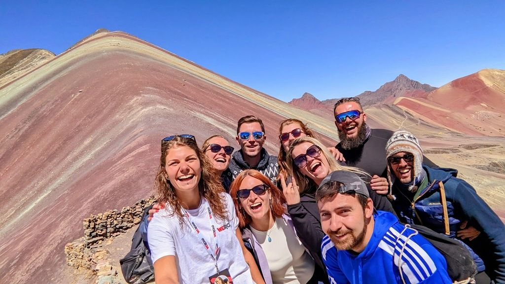 A happy group of WeRoad travelers posing for a selfie in front of Peru's Rainbow Mountain.