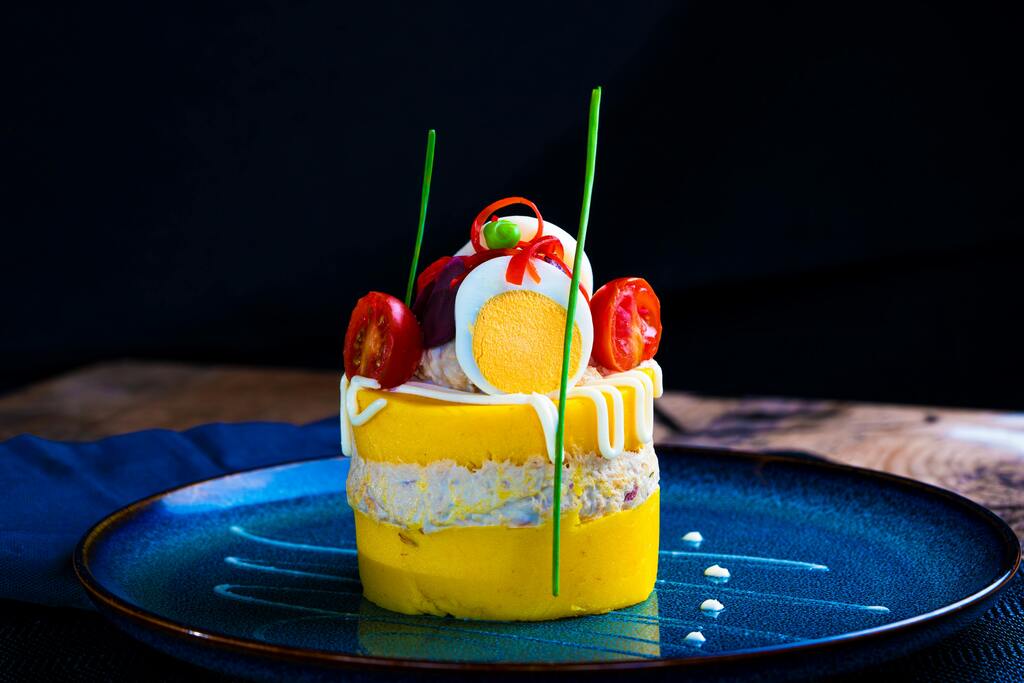 Causa limeña, a Peruvian layered potato dish with a creamy filling, garnished with tomatoes, eggs, and green onions.
