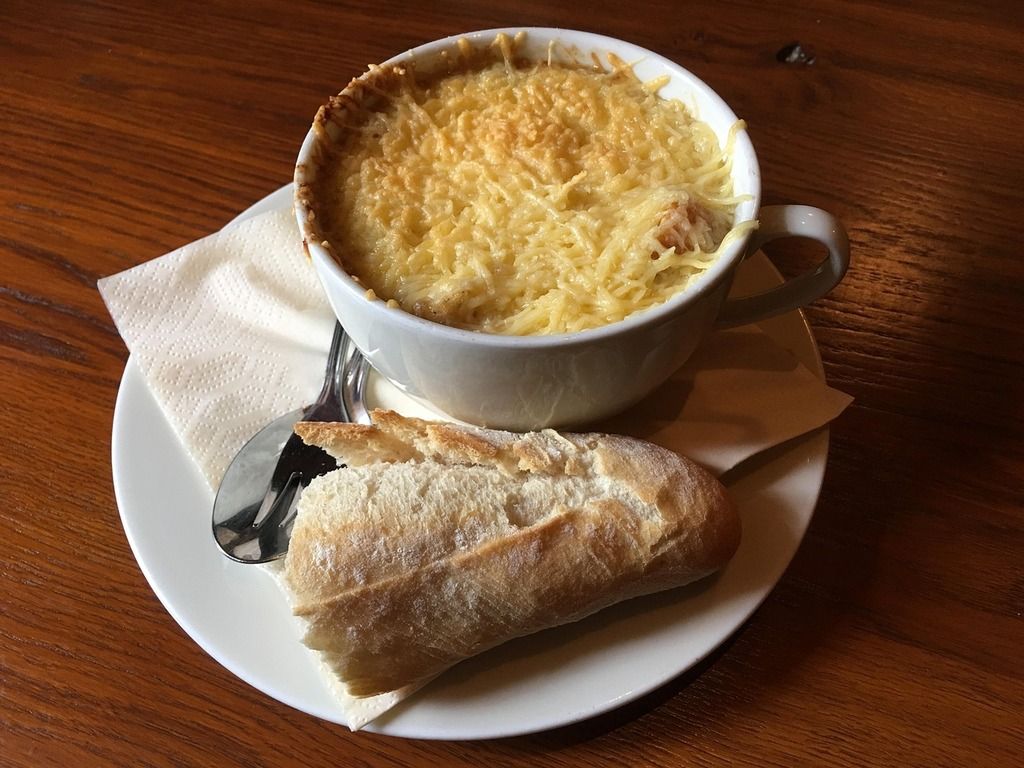 A bowl of French Soupe à l'oignon topped with melted cheese, served with a slice of crispy bread