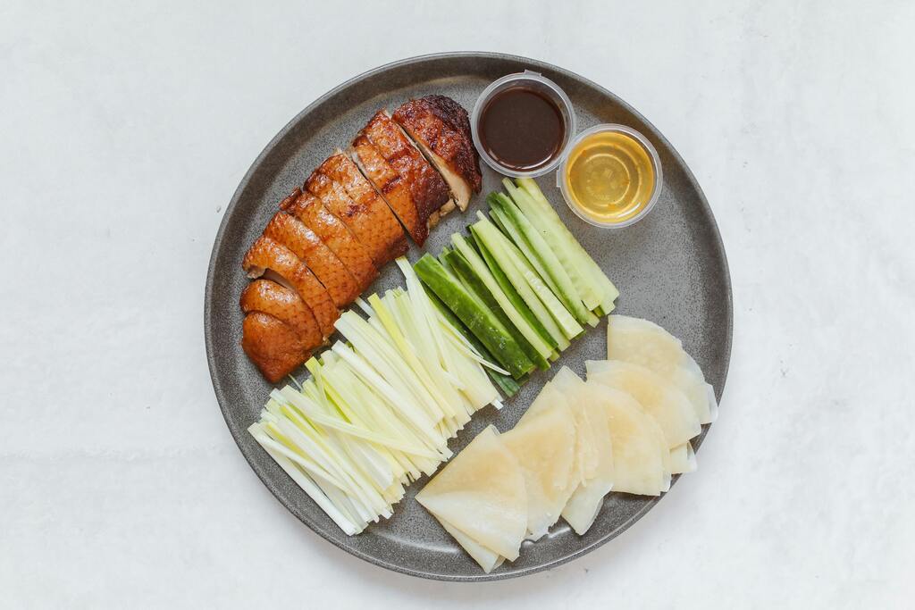 A plate of traditional Peking duck with cucumber, scallions, pancakes, and dipping sauces, a famous Chinese delicacy.
