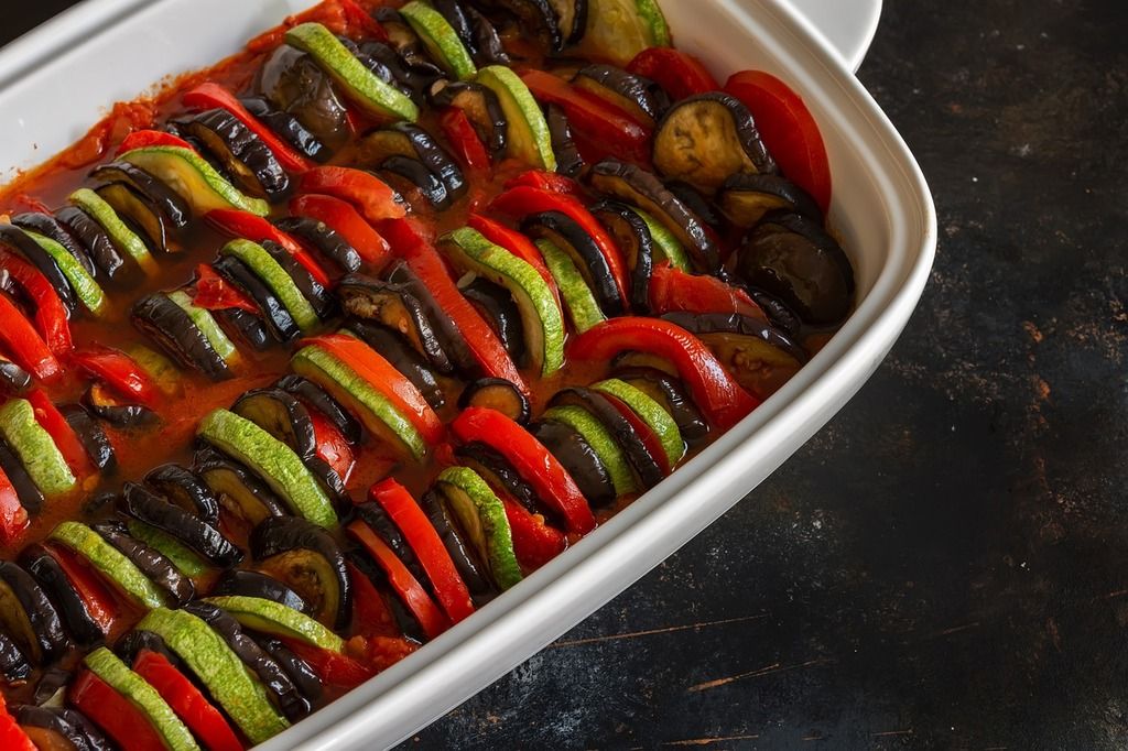 A delicious baked ratatouille with zucchini, eggplant, and bell peppers arranged in a white dish.