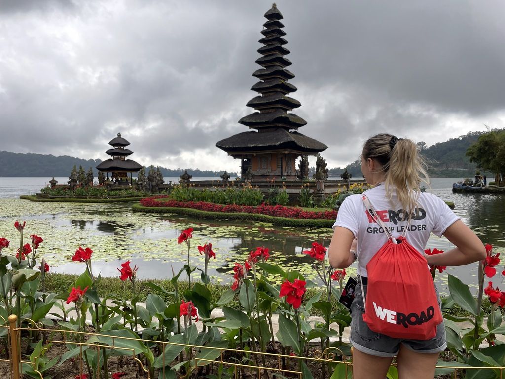 WeRoad traveler exploring Bali's Ulun Danu Beratan Temple, surrounded by beautiful lotus flowers and lake reflections.