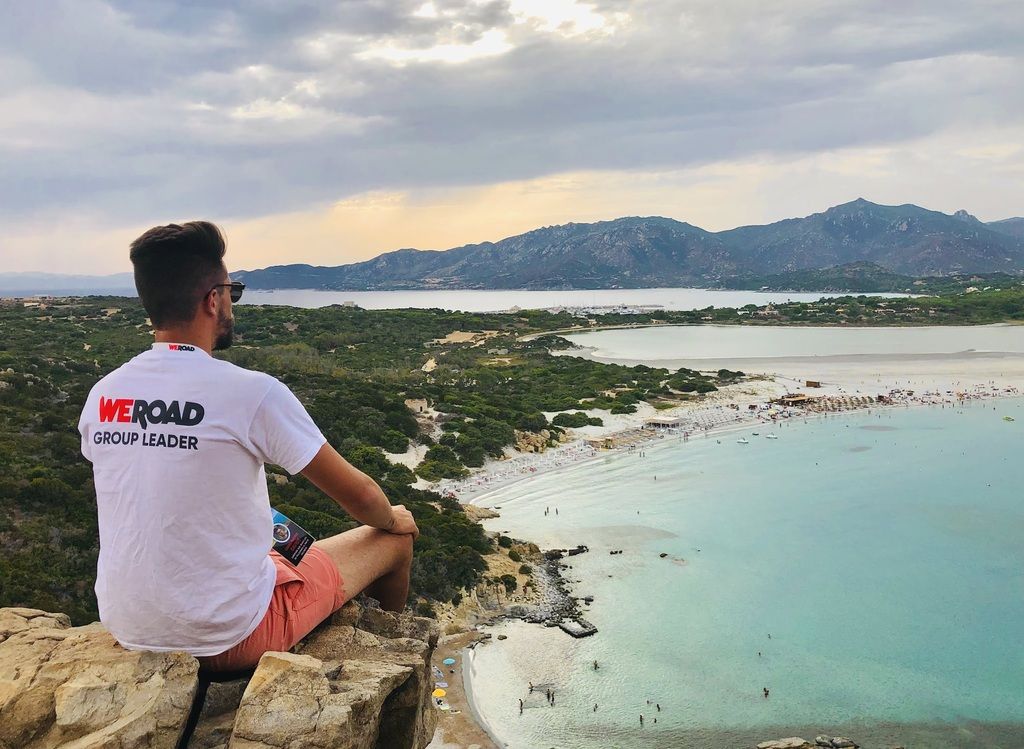WeRoad group leader enjoying a panoramic view of a stunning beach and crystal-clear waters from a cliffside.