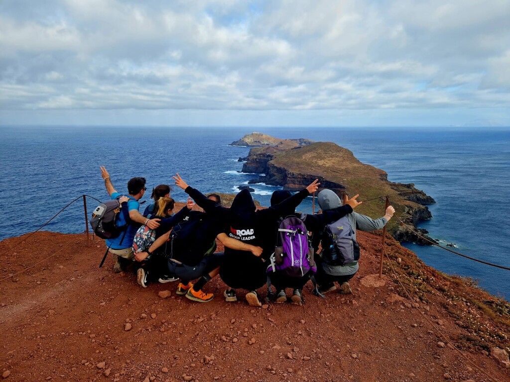 Group of WeRoad hikers sitting on a cliff overlooking a breathtaking coastal landscape.