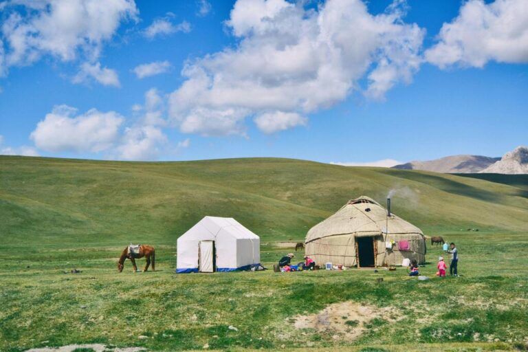 Yurts and tent in a green Kyrgyz mountain pasture with horses.