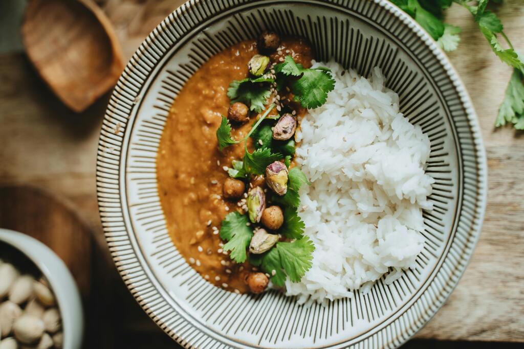 Indian curry dish with white rice, garnished with chickpeas, pistachios, and cilantro in a ceramic bowl