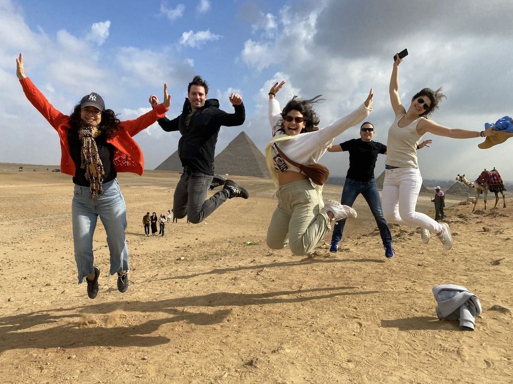 WeRoad group jumping in the air in front of the Giza pyramids in the Egyptian desert.