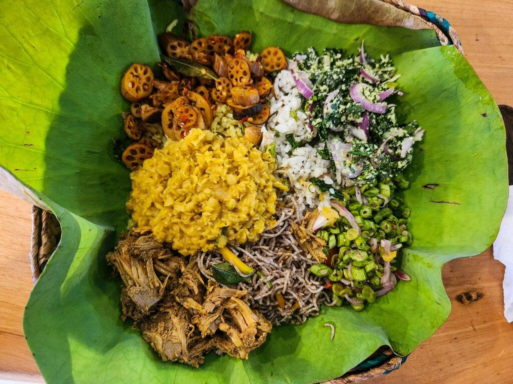 Traditional Sri Lankan meal served on a lotus leaf, featuring rice, lentils, jackfruit curry, string hoppers, and vegetables