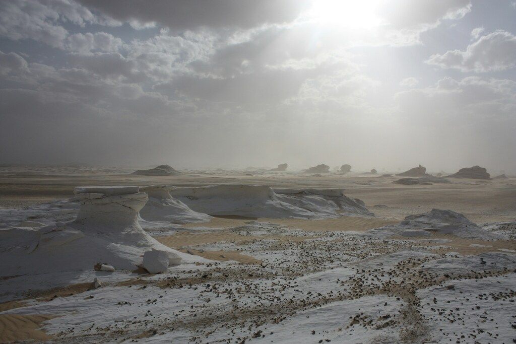 Dramatic view of the White Desert in Egypt with unique chalk rock formations and cloudy sky.