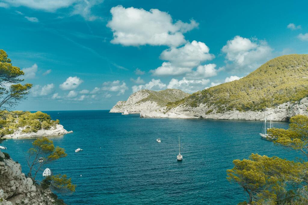 Boats anchored in a secluded bay with cliffs and pine trees in Balearic Islands