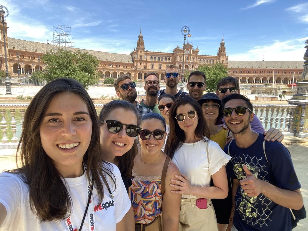 A group of smiling WeRoad travelers taking a selfie in front of the historic Plaza de España in Seville