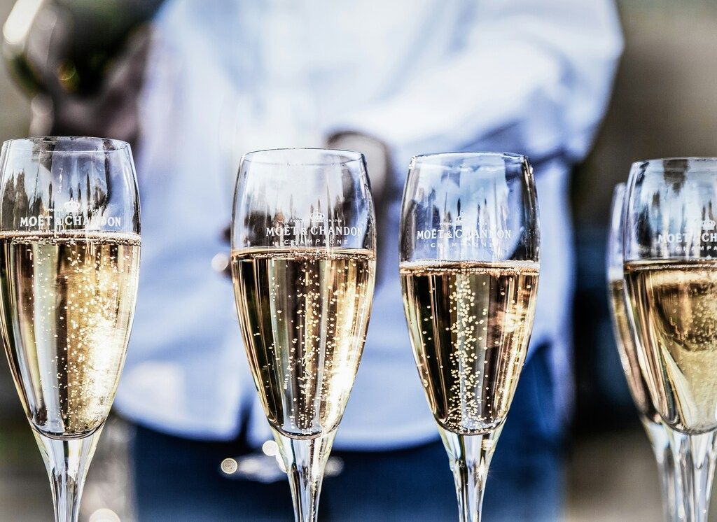 Several flute glasses filled with sparkling champagne, showing bubbles rising, with a blurred person in the background.