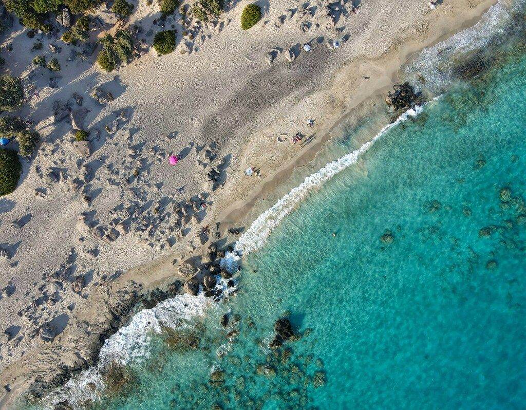 Top-down view of Kedrodasos Beach with umbrellas and people near clear turquoise sea