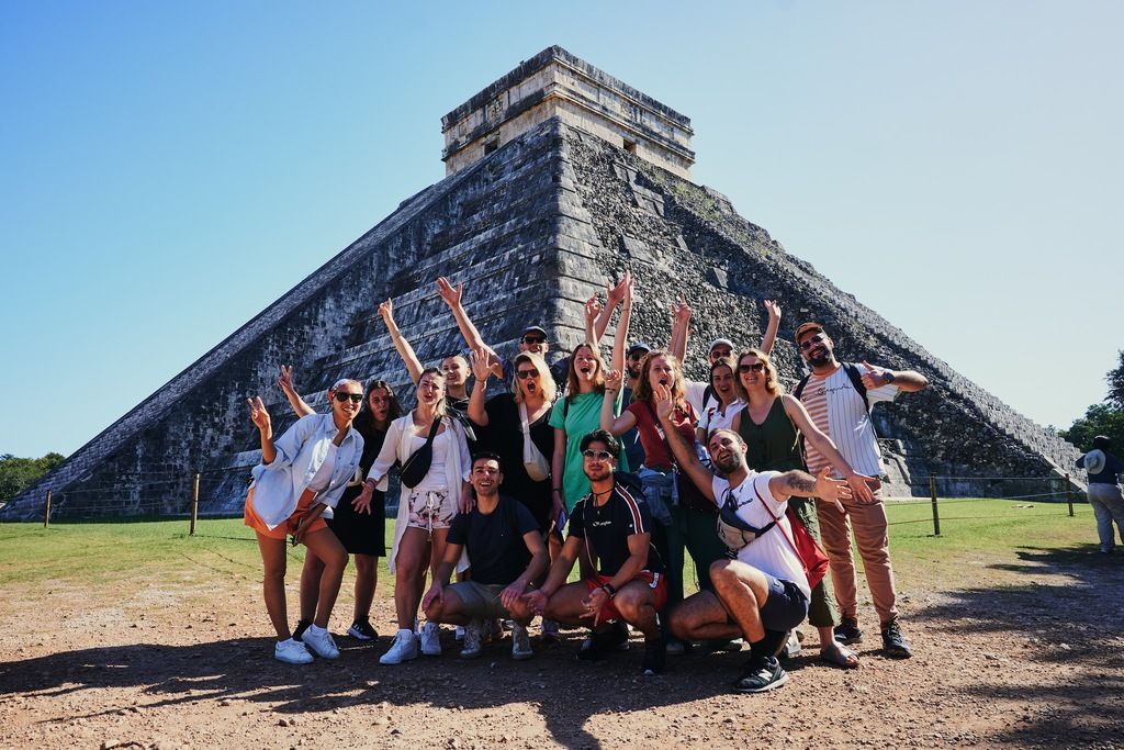 A large group of happy WeRoaders posing together in front of the Chichén Itzá pyramid in Mexico.