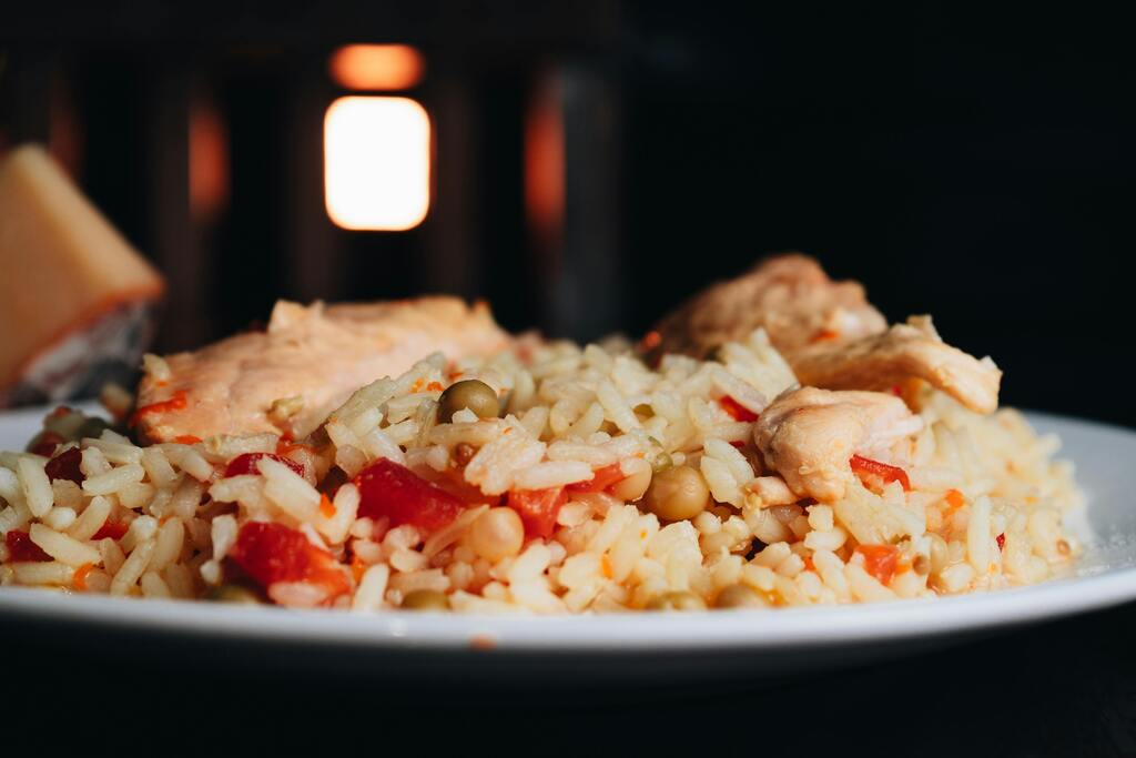 A close-up of a white plate with Arroz con Pollo, featuring rice, chicken pieces, peas, and red peppers.