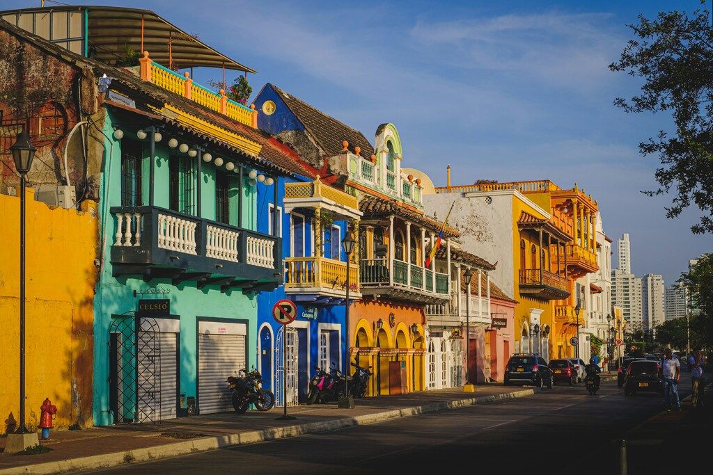 A colorful street scene in Cartagena, Colombia, with vibrant colonial buildings featuring balconies and a few cars and people on the street..