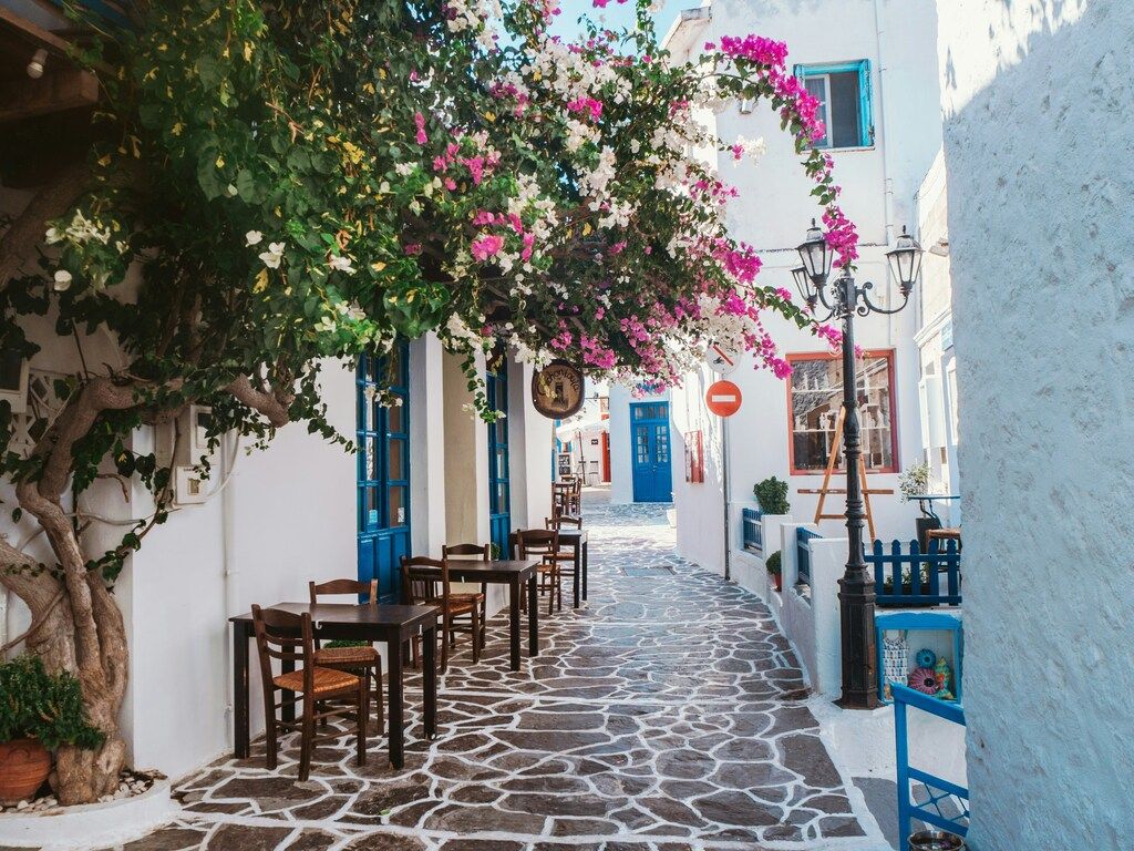 A charming narrow street in a Greek island village with whitewashed buildings, blue doors, and vibrant pink bougainvillea.