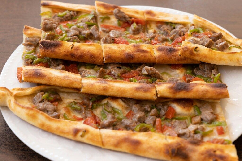 Slices of Turkish pide (flatbread) topped with meat, green peppers, and tomatoes on a white plate.